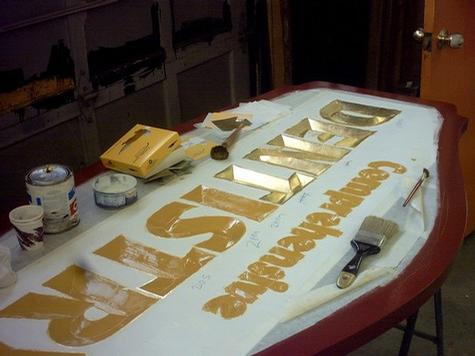 Applying the Gold Leaf to Carved Sign — sign being fabricated on the bench by Hale Custom Signs